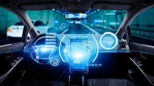 A driver's view of a holographic driverless vehicle dashboard where the words 'self-driving' can be seen.