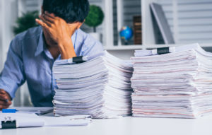 Young asian exhausted businesssman with messy desk and stack of