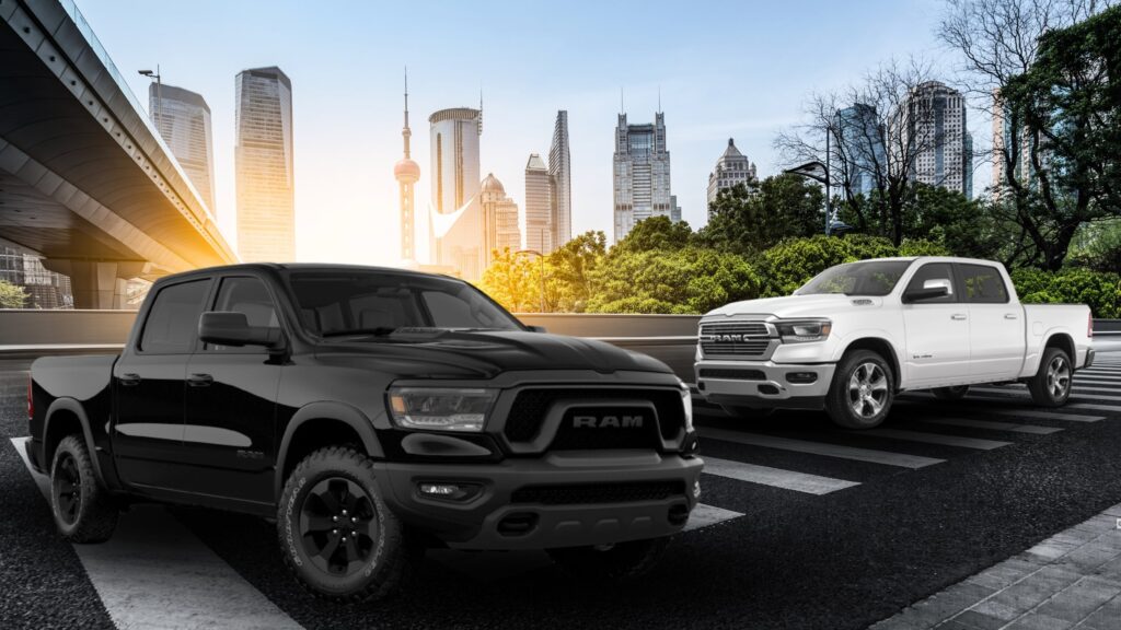 A black Ram truck in the left foreground and a white Ram truck on the right, parked on a sunny city street.