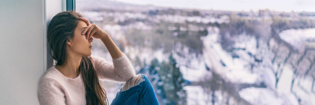 Winter depression sad woman with Seasonal affective disorder girl grief stricken alone at home window thinking negative thoughts. Mental health banner panorama background.