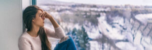 Winter depression sad woman with Seasonal affective disorder girl grief stricken alone at home window thinking negative thoughts. Mental health banner panorama background.