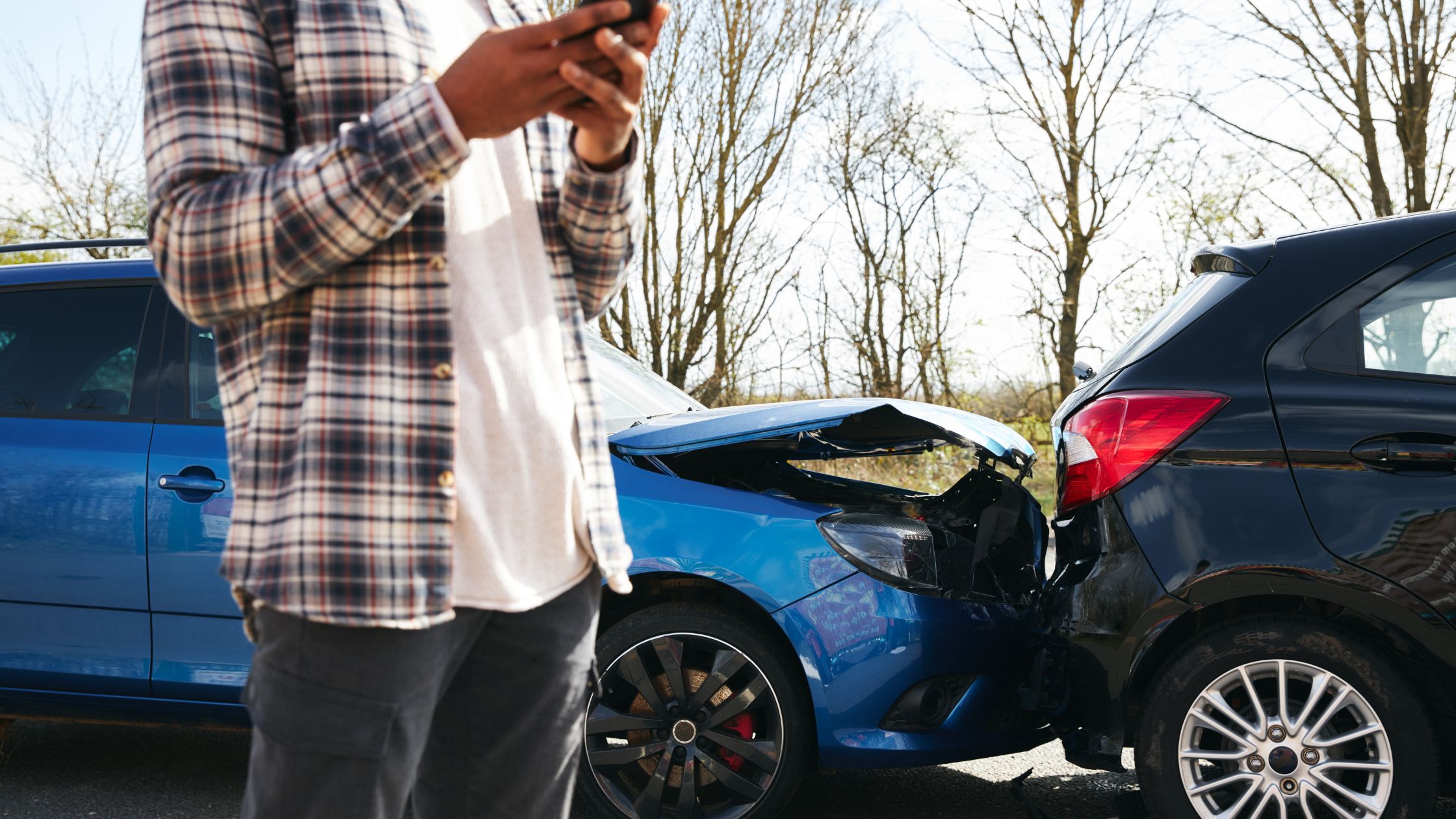 A driver texts in the foreground in front of a car accident.