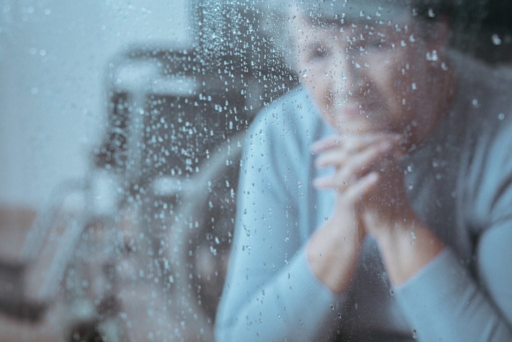 Depressed Senior Citizen behind rainy window