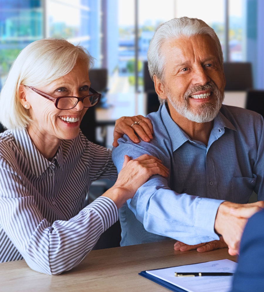 senior woman and senior man sitting at table and man shaking hands with another person